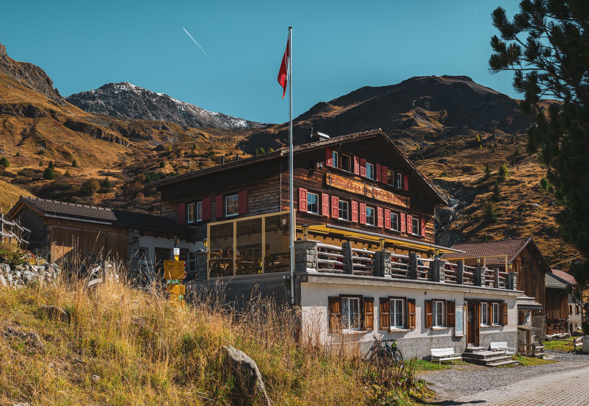 Rustic chalet in Surses, Switzerland with stunning mountain backdrop, clear blue skies, and autumn scenery. — photograph by Christopher Politano on Pexels