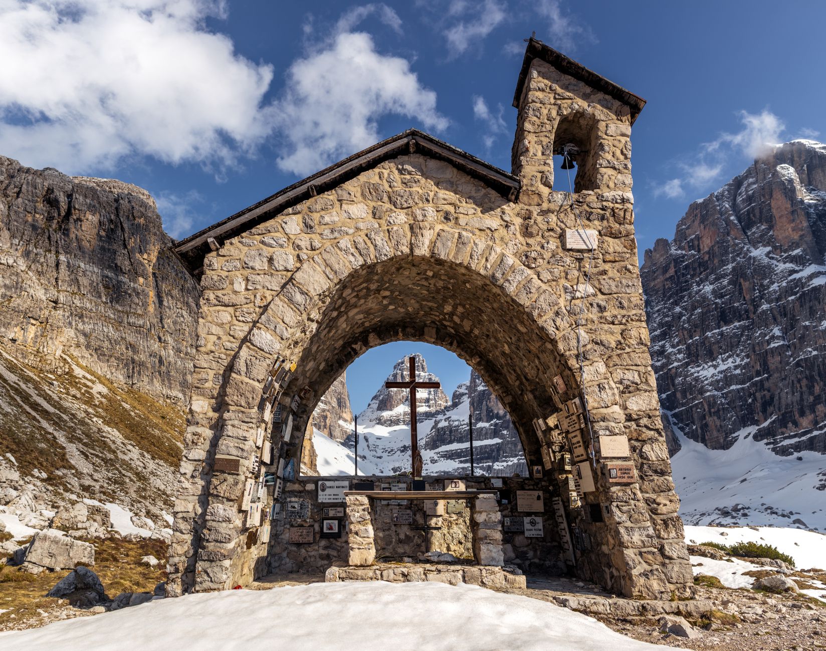 Stone chapel with cross in Madonna di Campiglio, Italy, surrounded by snowy mountains. — photograph by Marek Piwnicki on Pexels