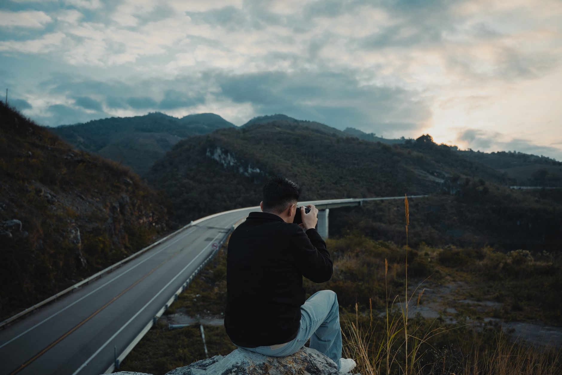 A photographer sits on a rock, taking pictures of a stunning mountain landscape in San Cristóbal de las Casas. — photograph by Frank Guzmán on Pexels