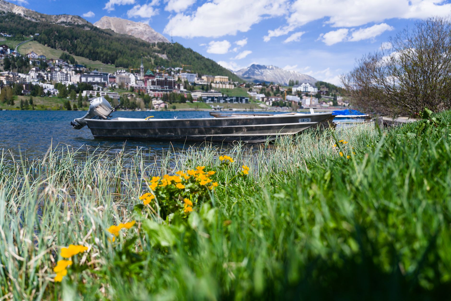 A boat rests by Lake St. Moritz with vibrant flowers and a stunning mountain backdrop. — photograph by Jean-Paul Wettstein on Pexels