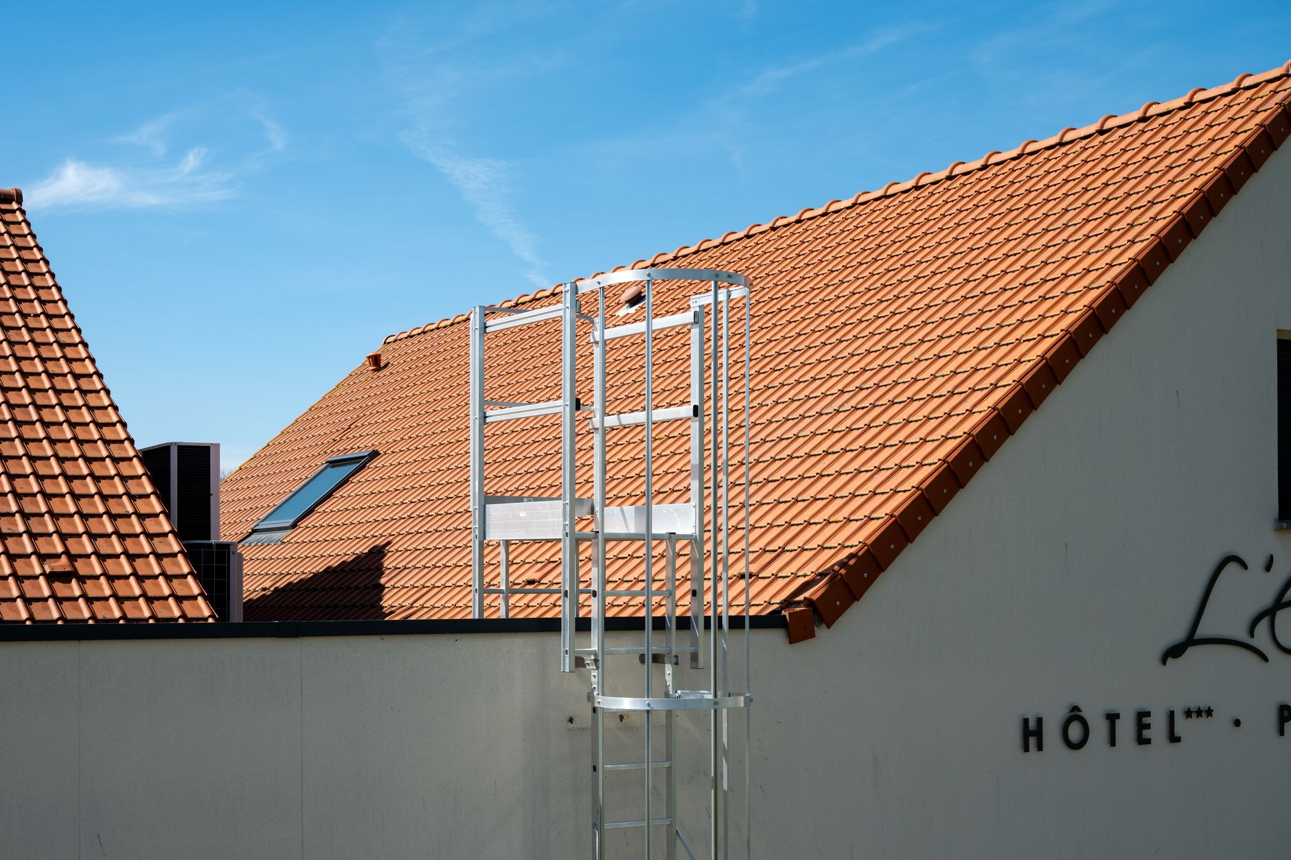 Sunny view of a hotel rooftop with ladder, featuring terracotta tiles and blue sky in Escalles, France. — photograph by Bingqian Li on Pexels